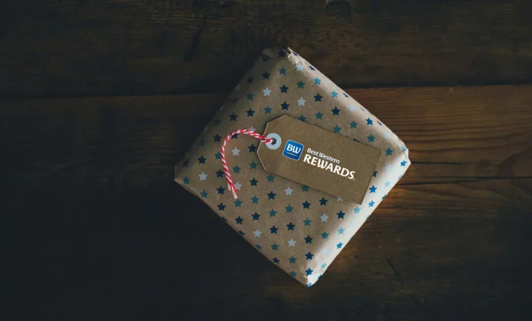 Nell'immagine, un primo piano su un pacchetto regalo poggiato su un tavolo in legno, sul quale è appesa un'etichetta con la scritta "Best Western Rewards".
